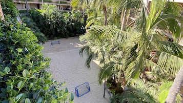 A courtyard with a sandy play area, surrounded by lush greenery and palm trees.