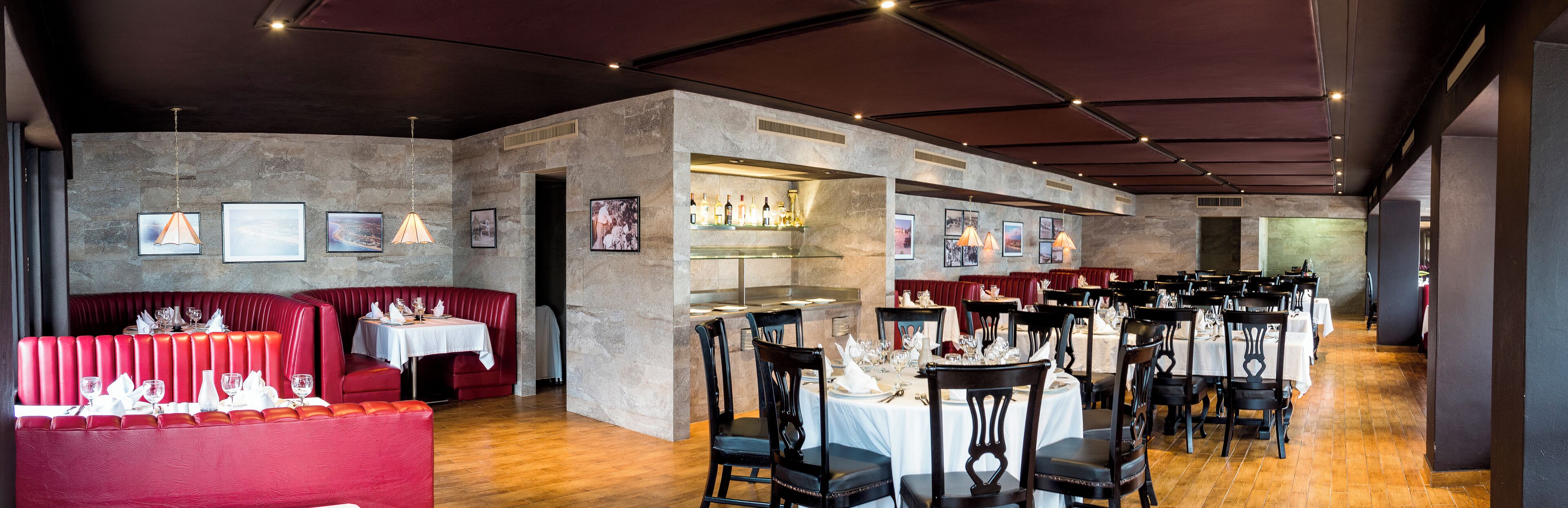 Un restaurant avec des banquettes rouges, un coin bar et plusieurs tables à manger avec des chaises.