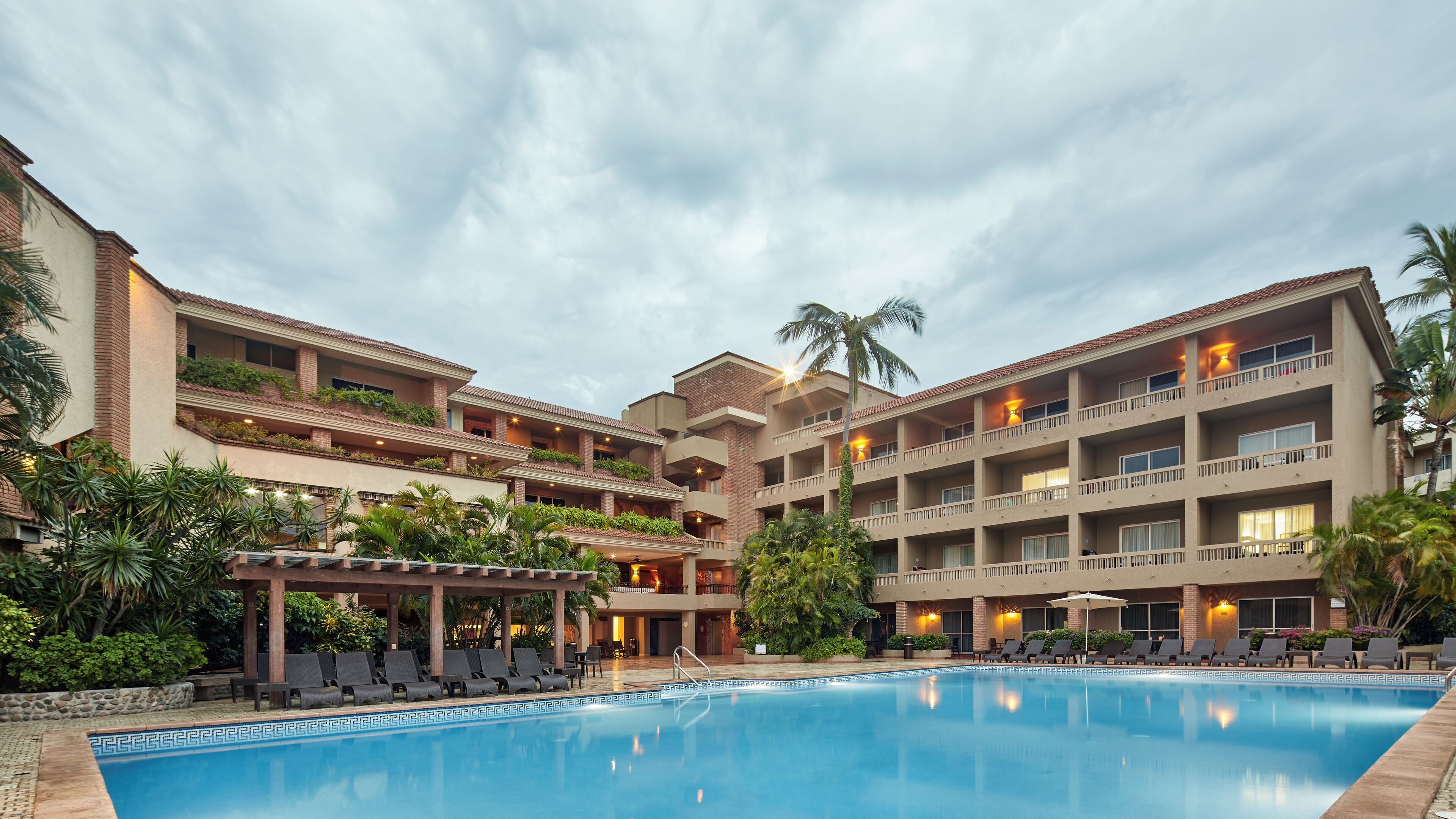 Ein Hotel mit Schwimmbad, mehreren Balkonen und üppiger Bepflanzung.