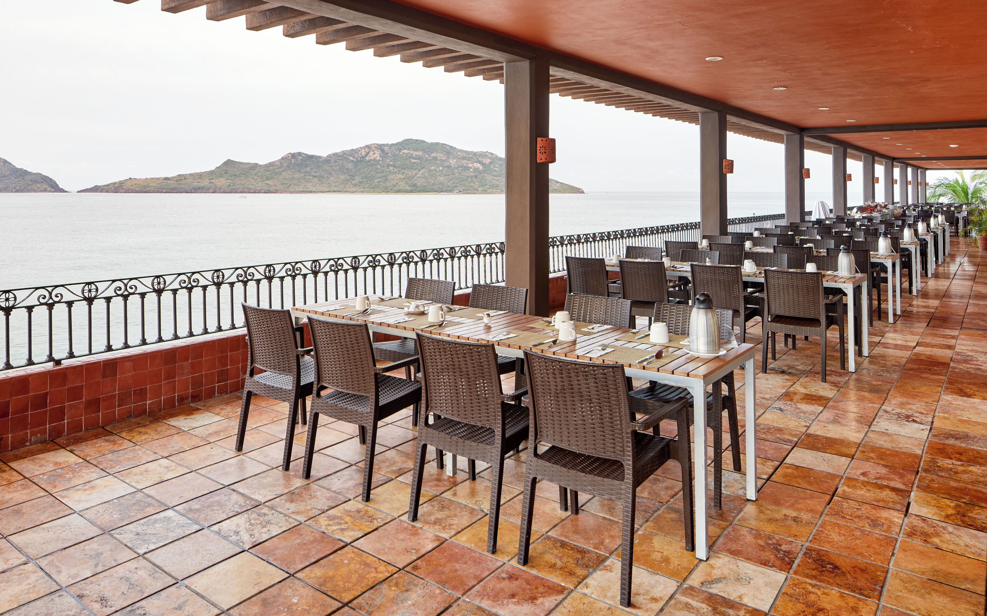 A seaside restaurant with outdoor seating, tables, and chairs, overlooking the ocean.
