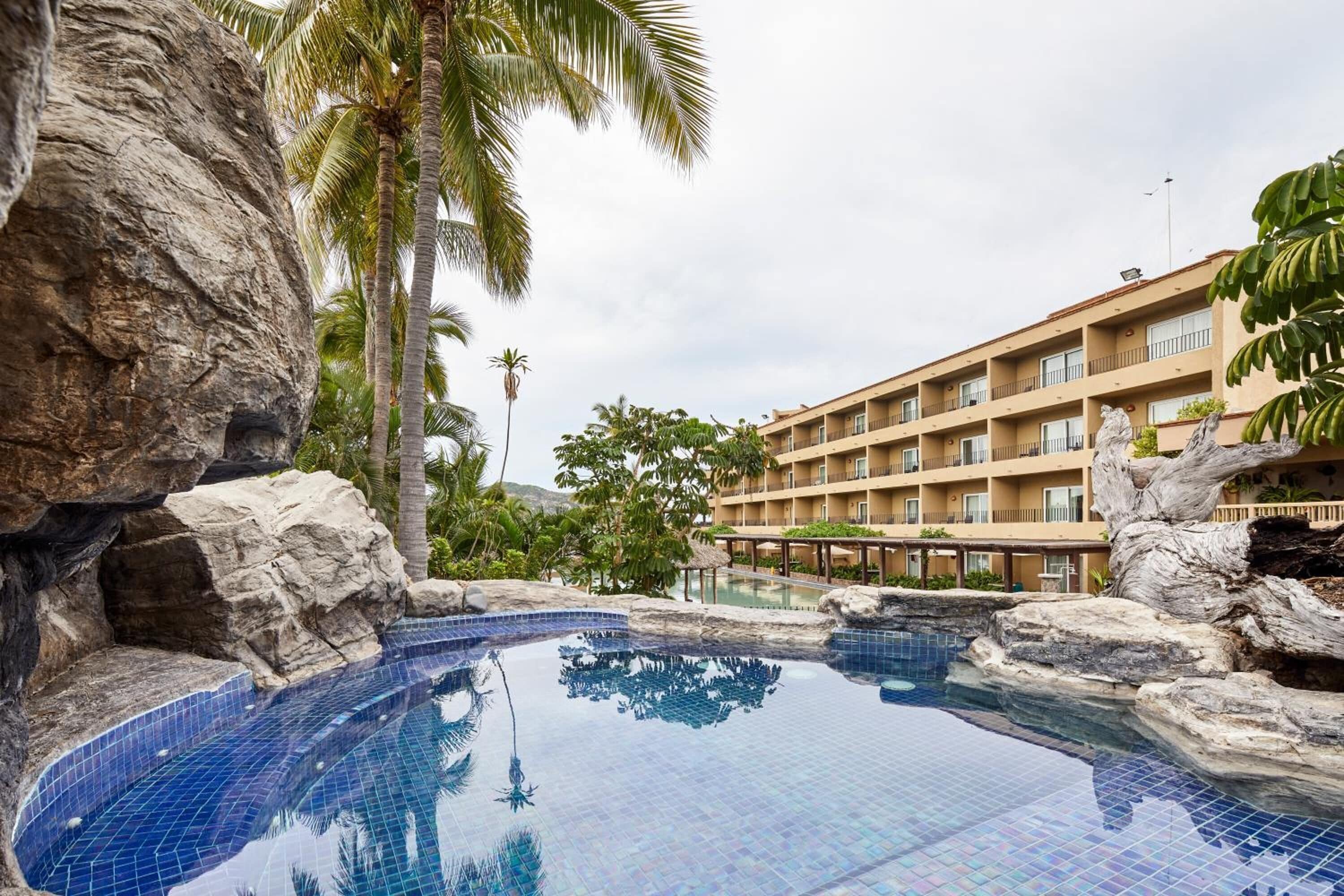 Un hotel con piscina rodeada de rocas y palmeras.