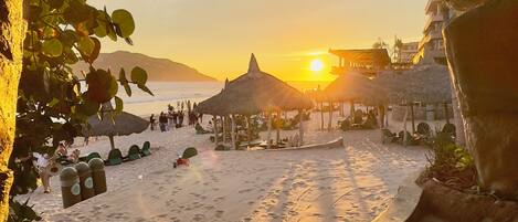 Een strandscène met rieten parasols en een ondergaande zon.