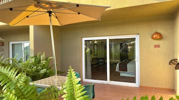 Una zona patio con tavolo e sedie, un ombrellone grande e una porta scorrevole in vetro che dà su un ambiente interno.