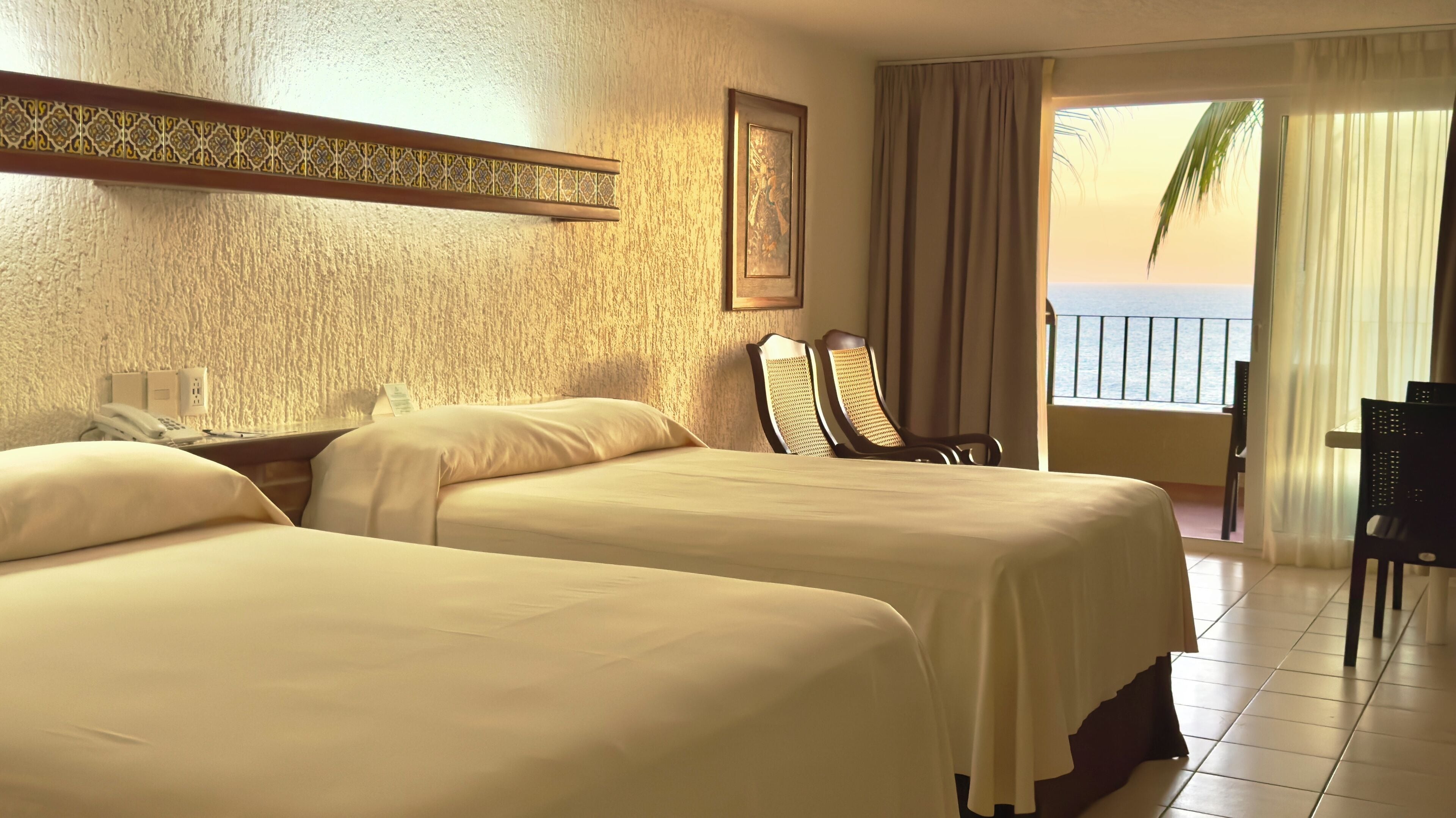 Ein Hotelzimmer mit zwei Betten, einem Schreibtisch mit Stuhl, einem Telefon und Blick auf das Meer.