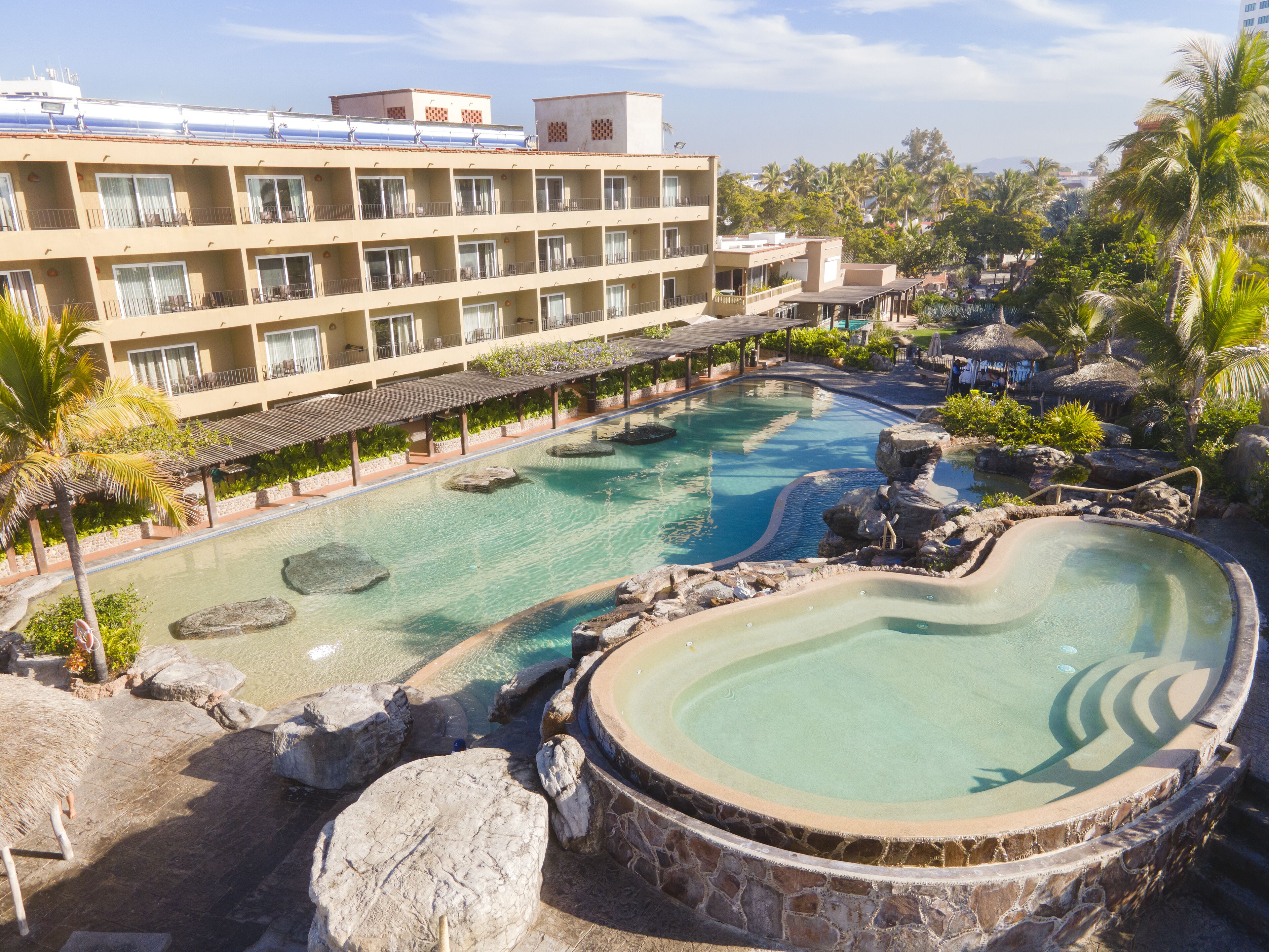 Un hôtel doté de nombreux balcons, d’une grande piscine agrémentée de rochers et d’un aménagement paysager de style tropical.