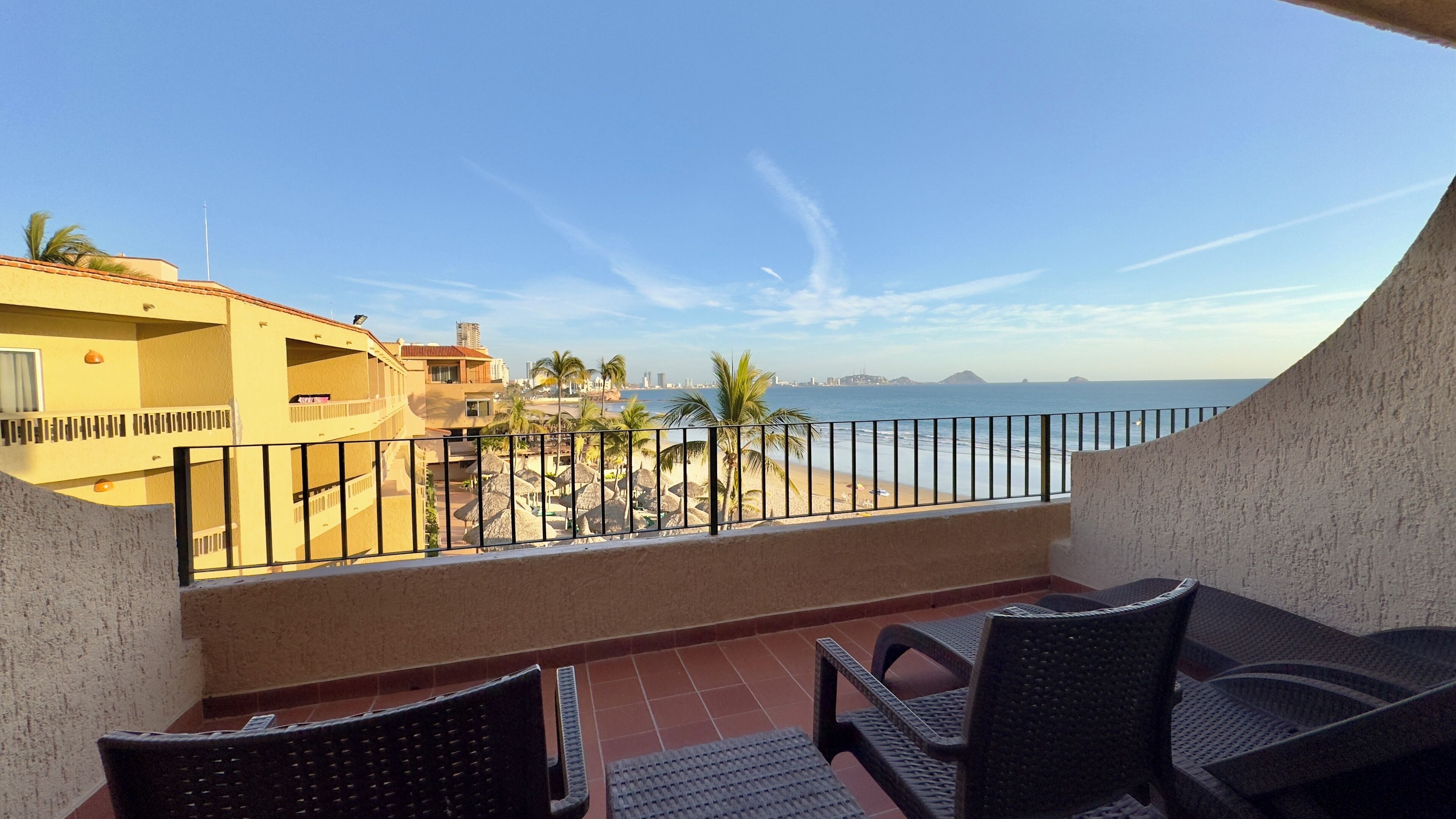 A balcony with a view of a beach and ocean, featuring a seating area with chairs and a table.
