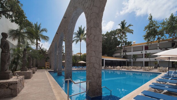A pool area with stone columns, lounge chairs, and palm trees. - El Cid Granada Hotel (Mazatlán)
