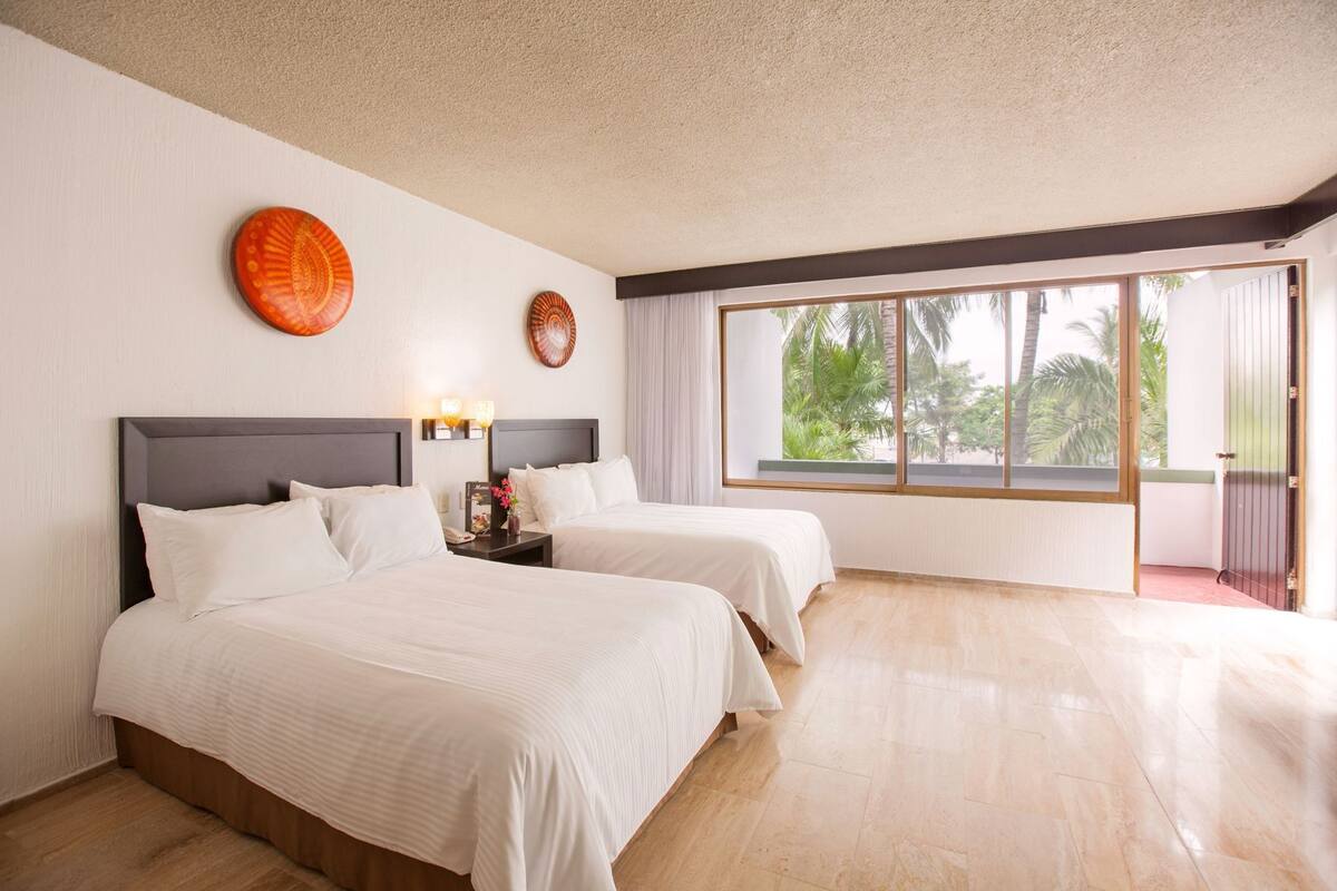 A hotel room with two beds, a large window, and a view of palm trees.