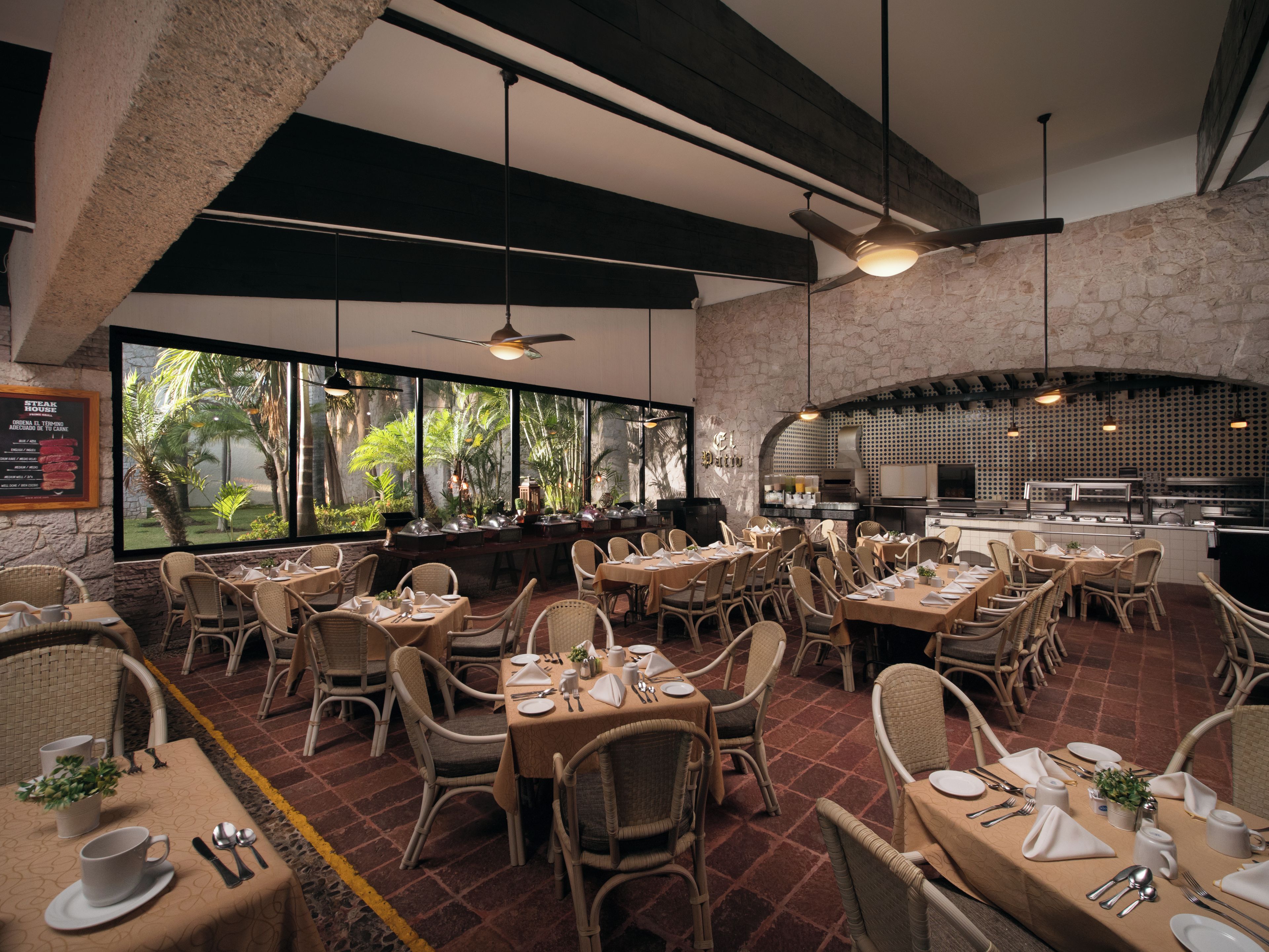 Un restaurant doté de nombreuses tables et chaises, d’un mur en pierre et offrant une vue sur la verdure grâce à de grandes fenêtres.