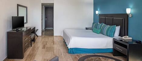 Een hotelkamer met een bed, nachtkastje, bureau, televisie en een plafondventilator.
