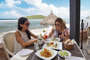 Dos personas cenando en una mesa al aire libre con vista al océano y a la playa.