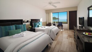 A hotel room with two beds, a desk with a television, a view of the sea, and a ceiling fan. - El Cid Castilla Beach Hotel (Mazatlán)