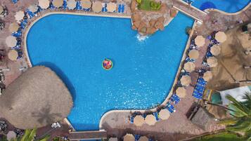 Une vue aérienne d’une piscine à l’eau bleue, entourée de chaises longues et de parasols, avec des palmiers et une petite cascade.