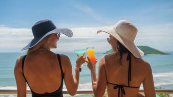 Two individuals at a seaside location, each holding a drink.