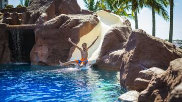 Slide into relaxation at this resort's pool, surrounded by natural rock formations and lush palm trees.