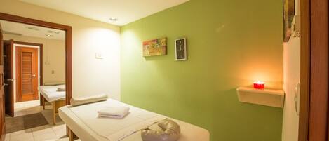 Una habitación con cama, mesa de masaje, un reloj de pared y un pequeño estante con una vela.
