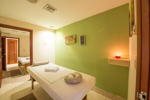 Una habitación con cama, mesa de masaje, un reloj de pared y un pequeño estante con una vela.