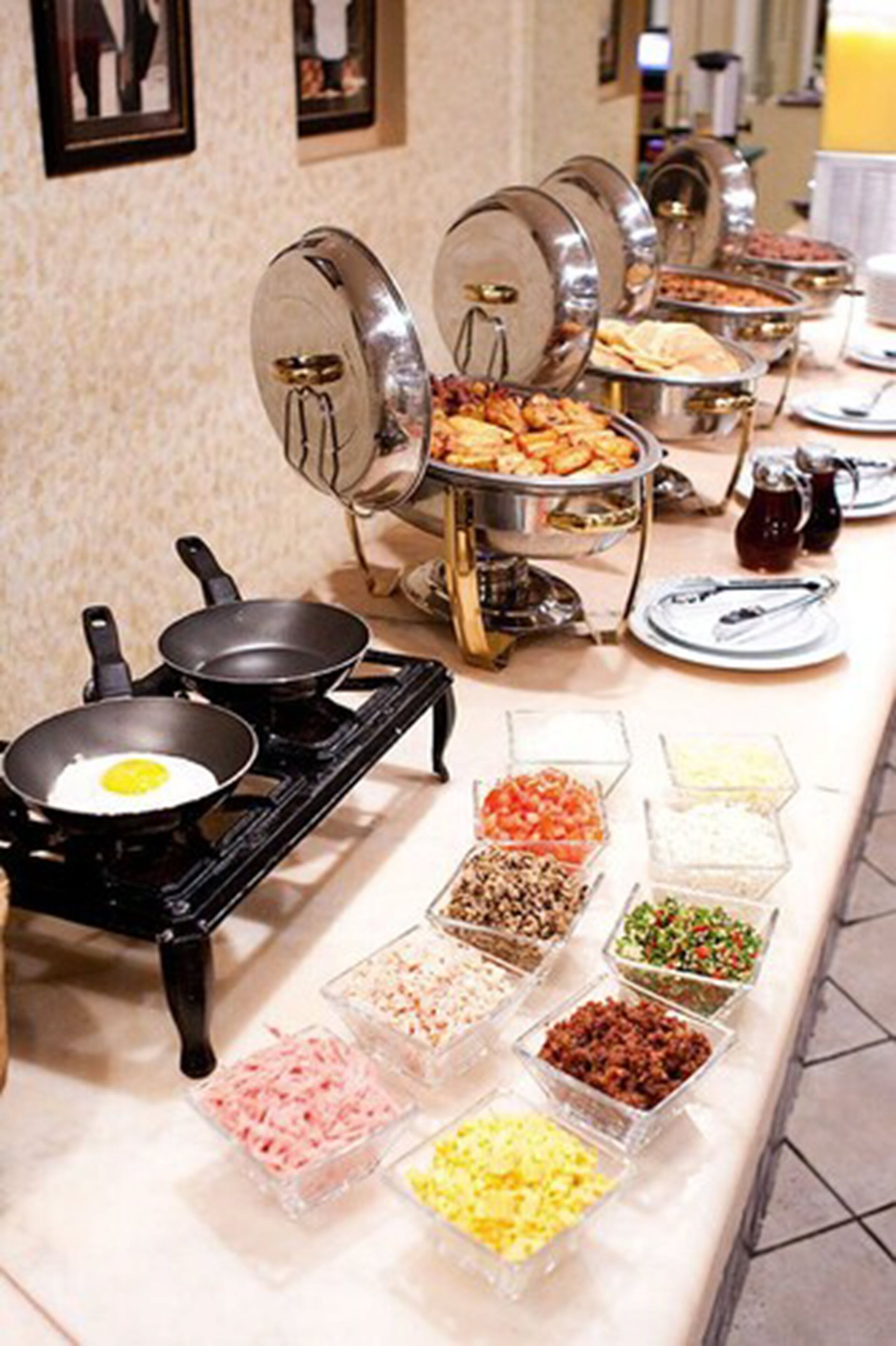 A buffet setup with various food containers and a stove with a frying pan.