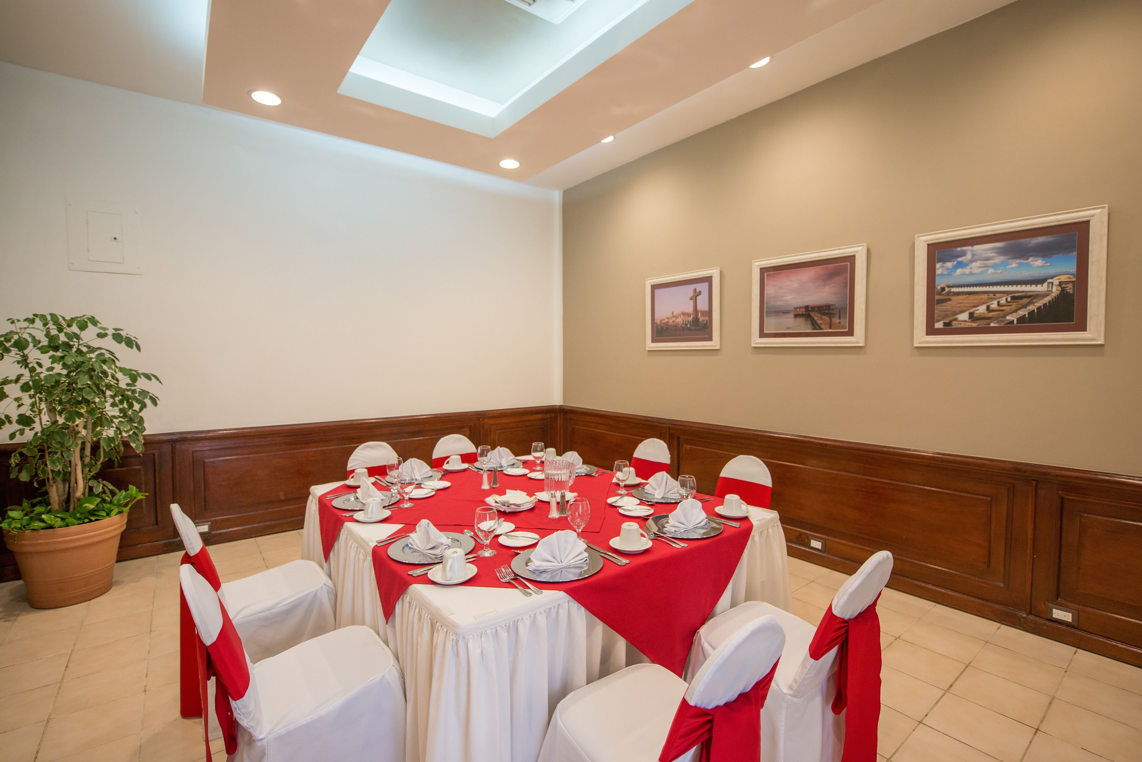 A conference room with a red tablecloth, white chairs, and framed pictures on the wall.