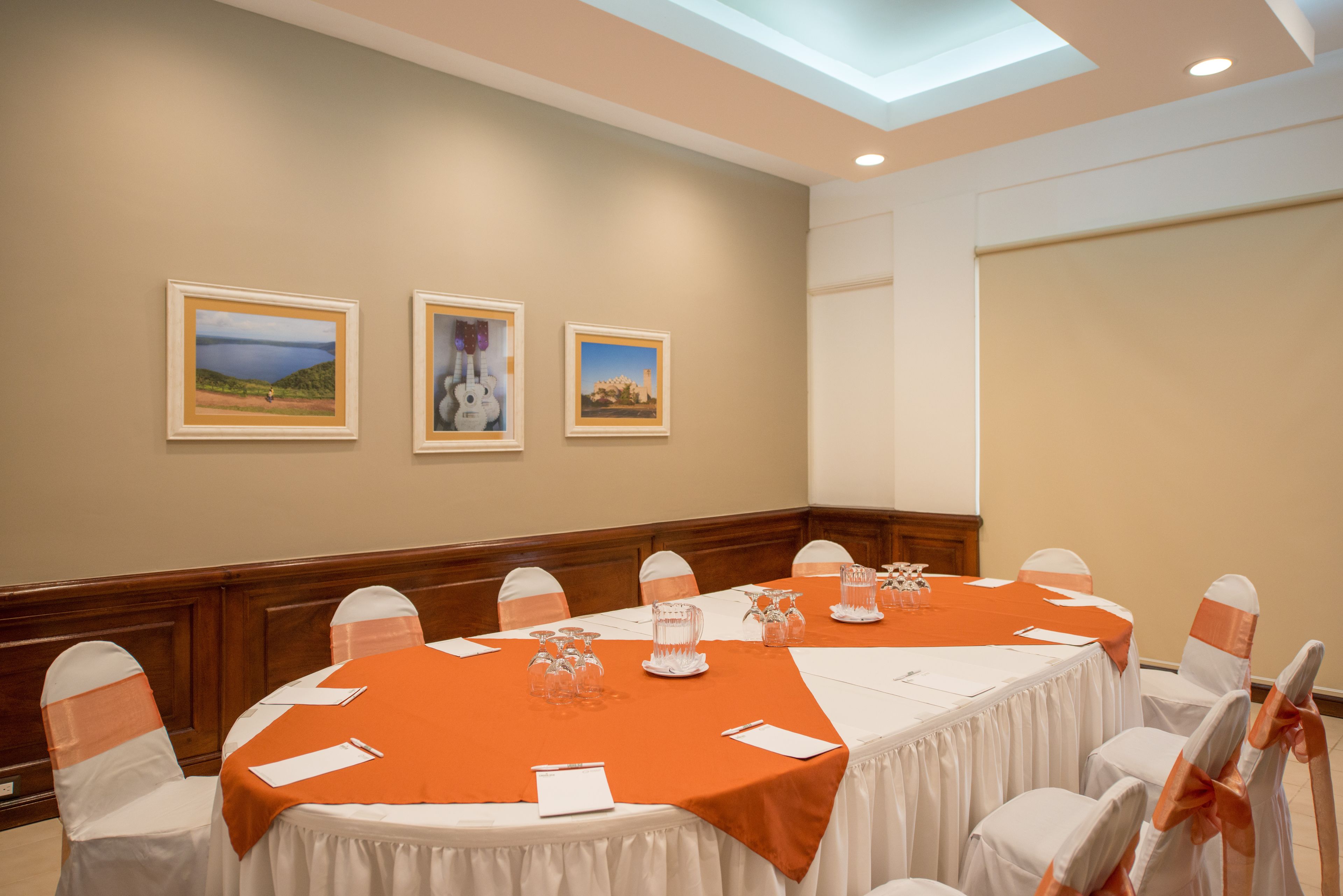 A conference room with a long table, white chairs with orange sashes, and framed pictures on the wall.