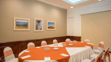 Une salle de conférence avec une longue table, des chaises blanches ornées de rubans orange et des tableaux encadrés accrochés au mur.