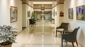 Ein Hotelkorridor mit poliertem Boden, gerahmten Kunstwerken an den Wänden und Sitzbereichen mit Stühlen und Tischen.