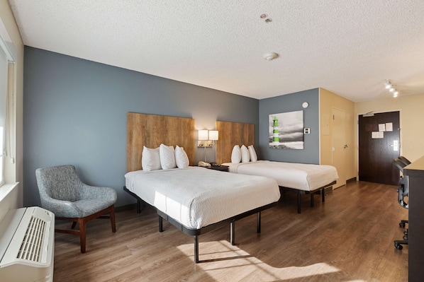 A hotel room with two beds, a chair, a desk, and a piano.
