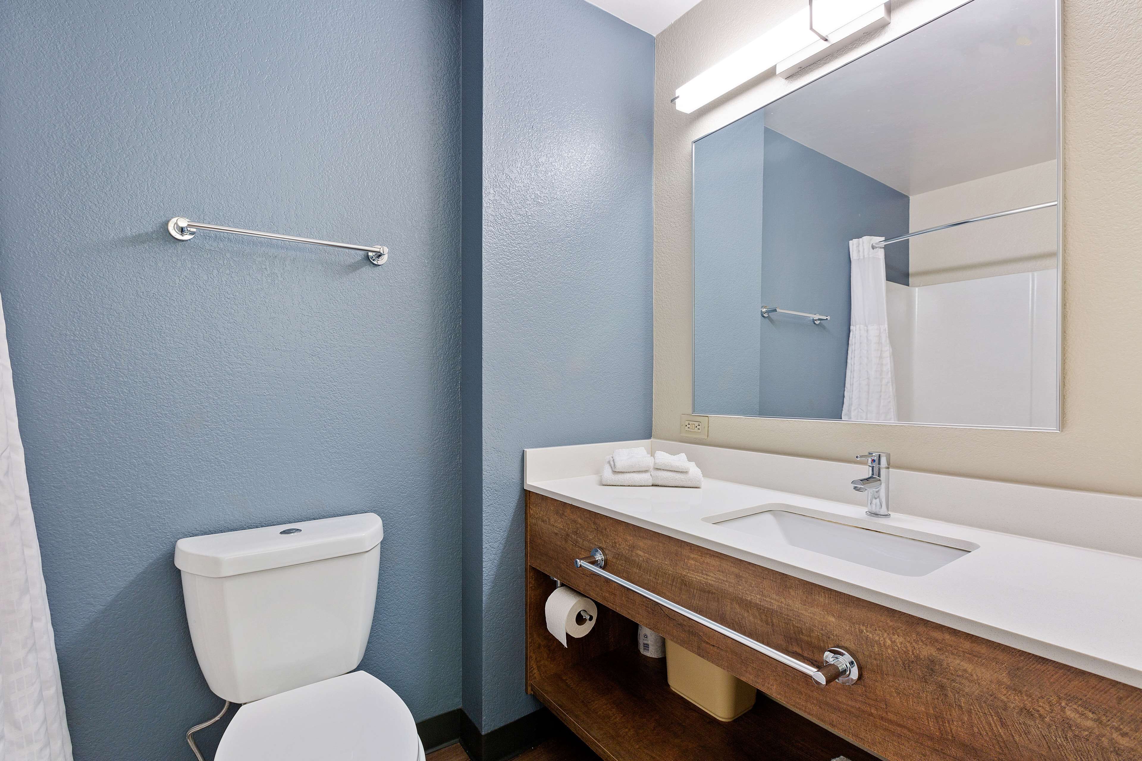 Ein Badezimmer mit Toilette, Waschbecken, Spiegel, Handtuchhalter und einer Handstange.