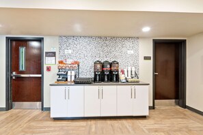 A reception area with a coffee station, a fire extinguisher, and a sign indicating the exit route.
