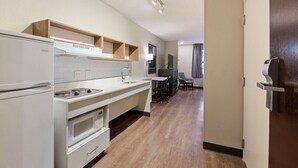 A modern kitchen with a refrigerator, stove, and microwave. There is a wooden shelf above the sink and a chair near the dining area. - Extended Stay America Premier Suites - Union City - Dyer St. (Union City)