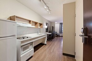 A modern kitchen with a refrigerator, stove, and microwave. There is a wooden shelf above the sink and a chair near the dining area.