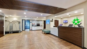 A reception area with a wooden floor, a reception desk, a seating area, a kitchenette, and a TV screen. - Extended Stay America Premier Suites - Union City - Dyer St. (Union City)
