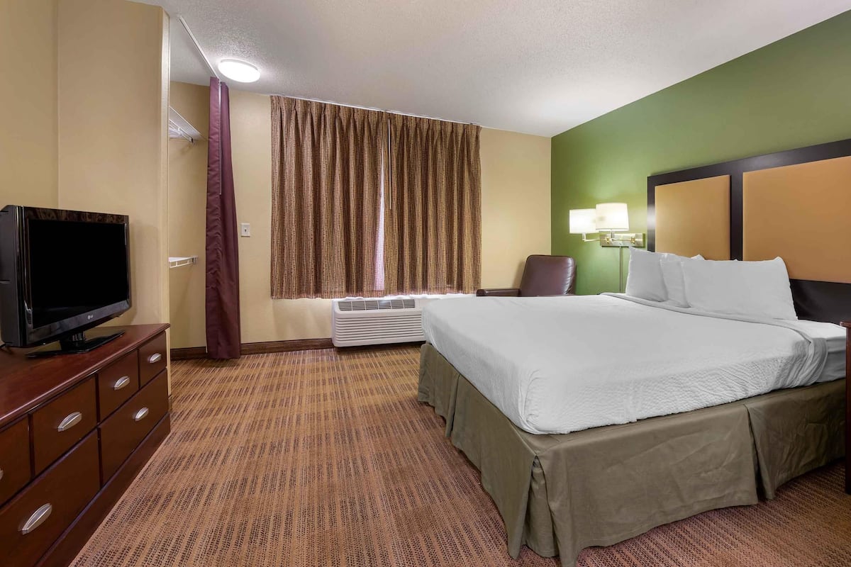 A hotel room with a bed, a television, a desk, a chair, a lamp, and a window with curtains.