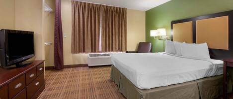 A hotel room with a bed, a television, a desk, a chair, a lamp, and a window with curtains.