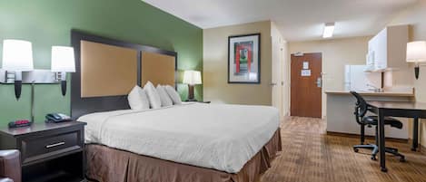 A hotel room with a large bed, bedside lamps, a desk with a chair, and a kitchenette.