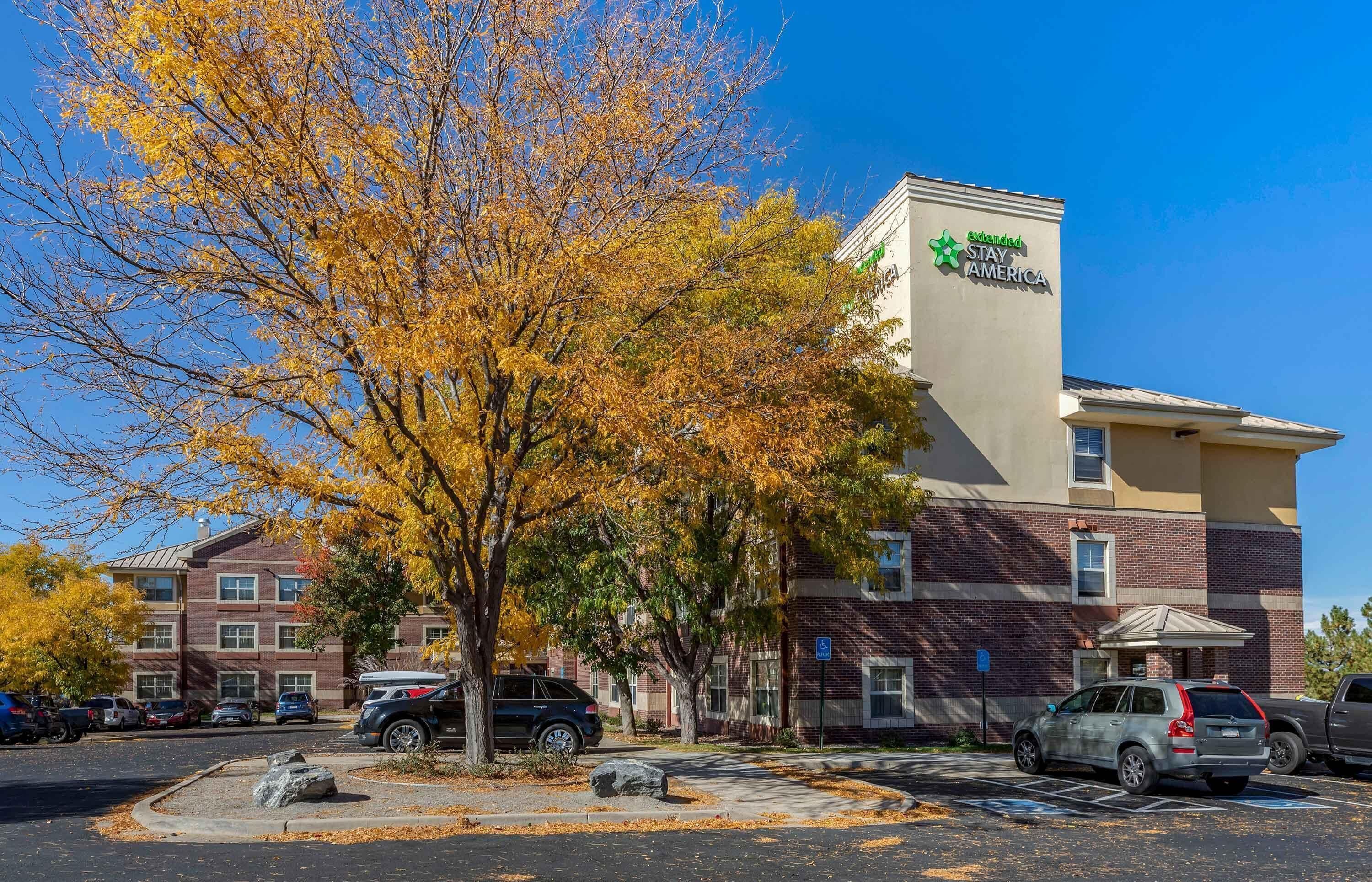 Un hotel con fachada de ladrillo, un letrero de Stay America y un estacionamiento con coches.