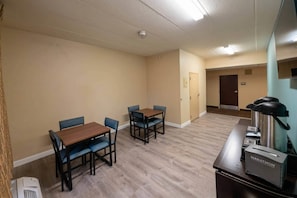 A hotel room with a wooden dining table, blue chairs, a kitchenette with a coffee maker, and a door leading to another room. - MainStay Suites Chicago Hillside (Hillside)