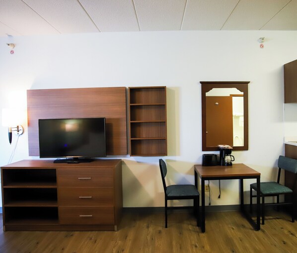 A hotel room with a TV, wooden shelving, a coffee maker, a desk, and two chairs.