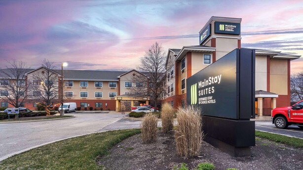 A MainStay Suites hotel with a large sign, a parking lot, and a building in the background. - MainStay Suites Chicago Hillside (Hillside)