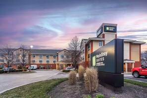 Ein MainStay Suites Hotel mit großer Schautafel, Parkplatz und einem Gebäude im Hintergrund.