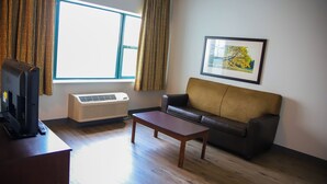 A living room with a sofa, a coffee table, a TV, and an air conditioner. - MainStay Suites Chicago Hillside (Hillside)