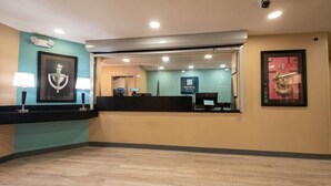 A reception area with a counter, two wall-mounted lamps, a framed artwork, and a sign for 'Mattress & Bedding.' - MainStay Suites Chicago Hillside (Hillside)