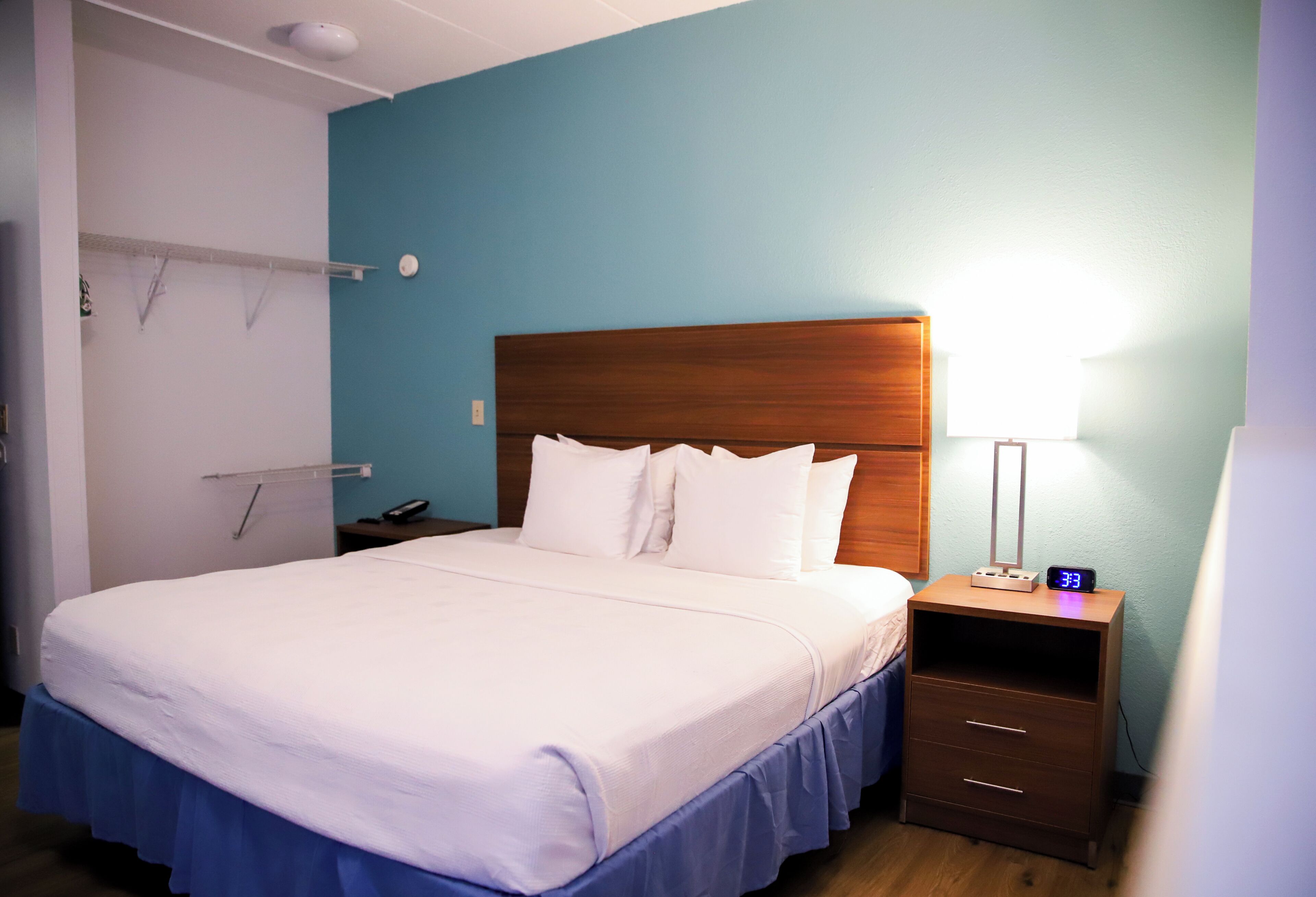 A hotel room with a large bed, a nightstand with a clock, and a wall-mounted towel rack.