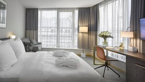 Une chambre d’hôtel comprenant un lit, un bureau avec une chaise, une télévision et de grandes fenêtres avec des rideaux.