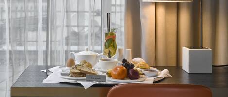 Uma mesa de café da manhã com uma chaleira, xícara, torradas, frutas e uma placa com a inscrição 'Bon appétit'.