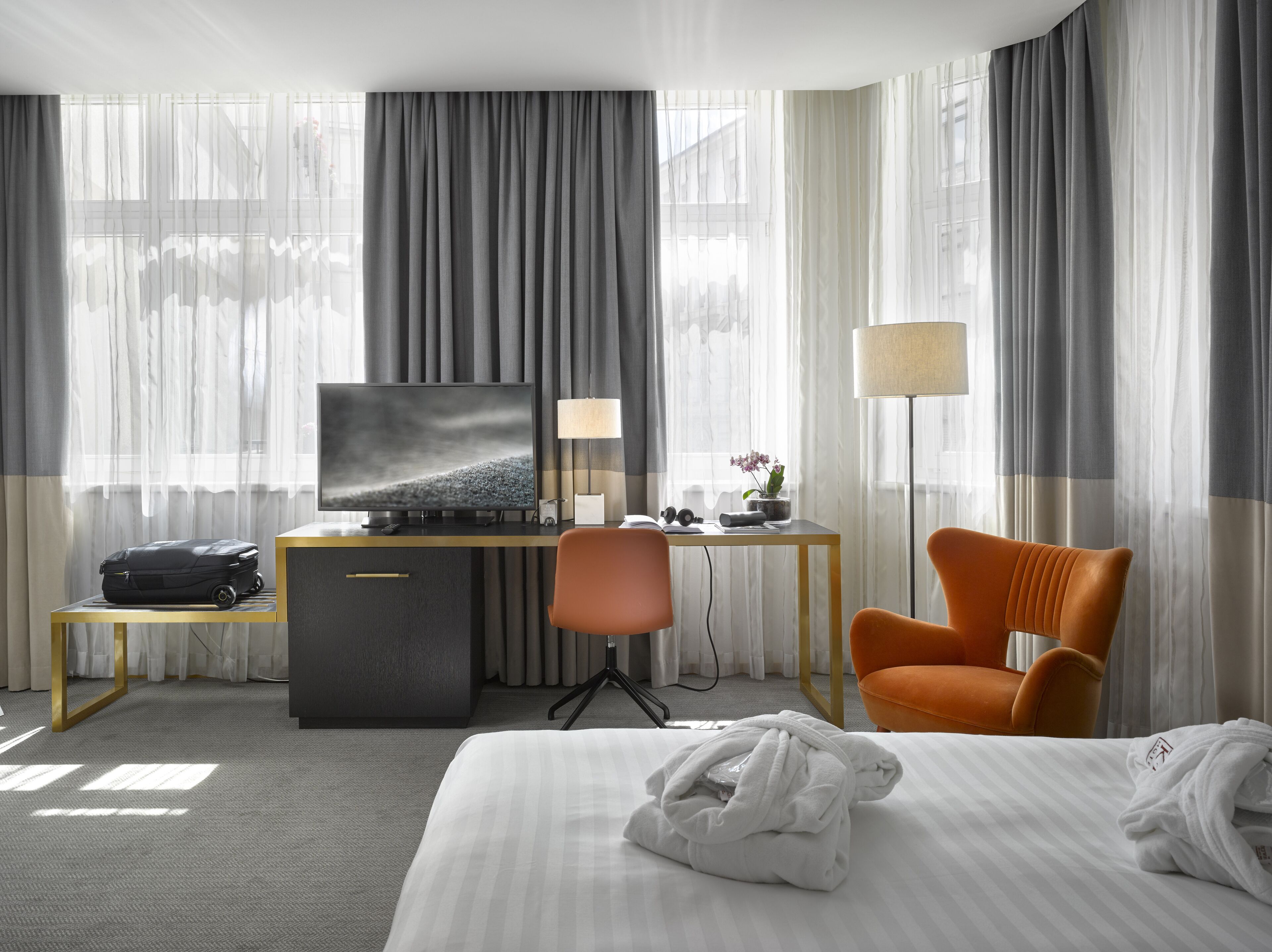 Quarto de hotel com cama, escrivaninha com televisão, cadeira e abajur.