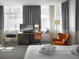 Quarto de hotel com cama, escrivaninha com televisão, cadeira e abajur.