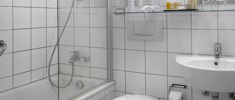 Un baño moderno con ducha envuelta en vidrio, inodoro blanco y lavamanos con espejo superior.