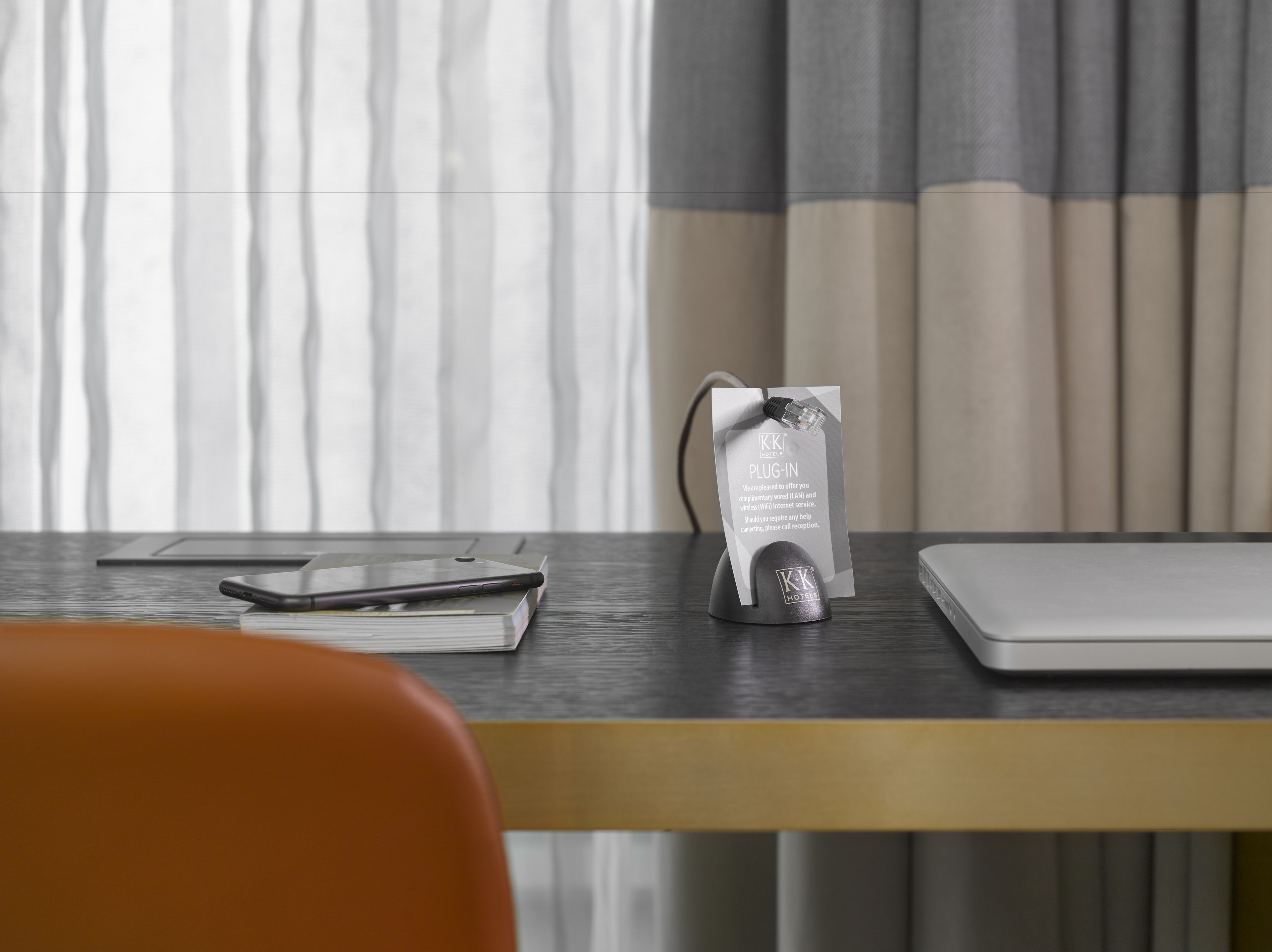 A hotel reception desk with a laptop, a smartphone, and a plug-in station.