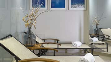 Relax in a serene space with a glass partition separating the seating area, featuring two lounge chairs and a large mirror reflecting the room's tranquil ambiance.